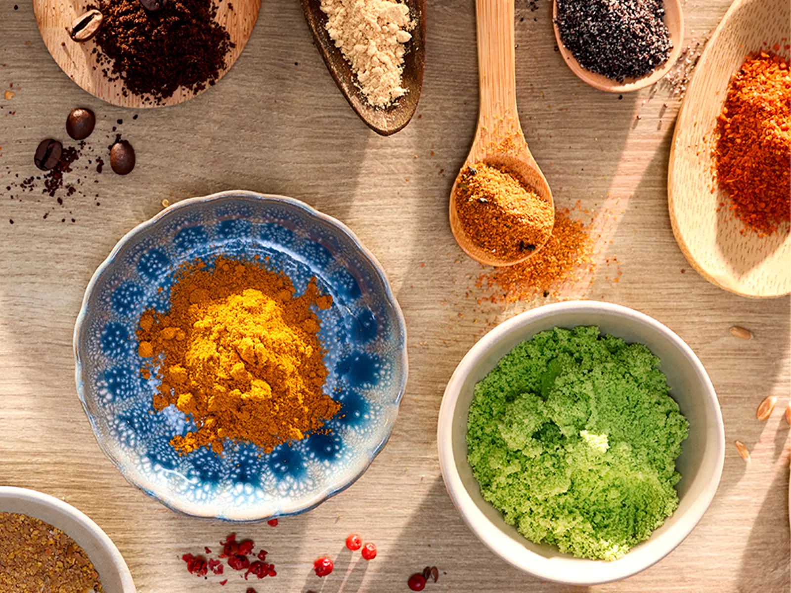 Boluri şi linguri din lemn cu mirodenii şi condimente asortate, aşezate pe o suprafaţă din lemn.