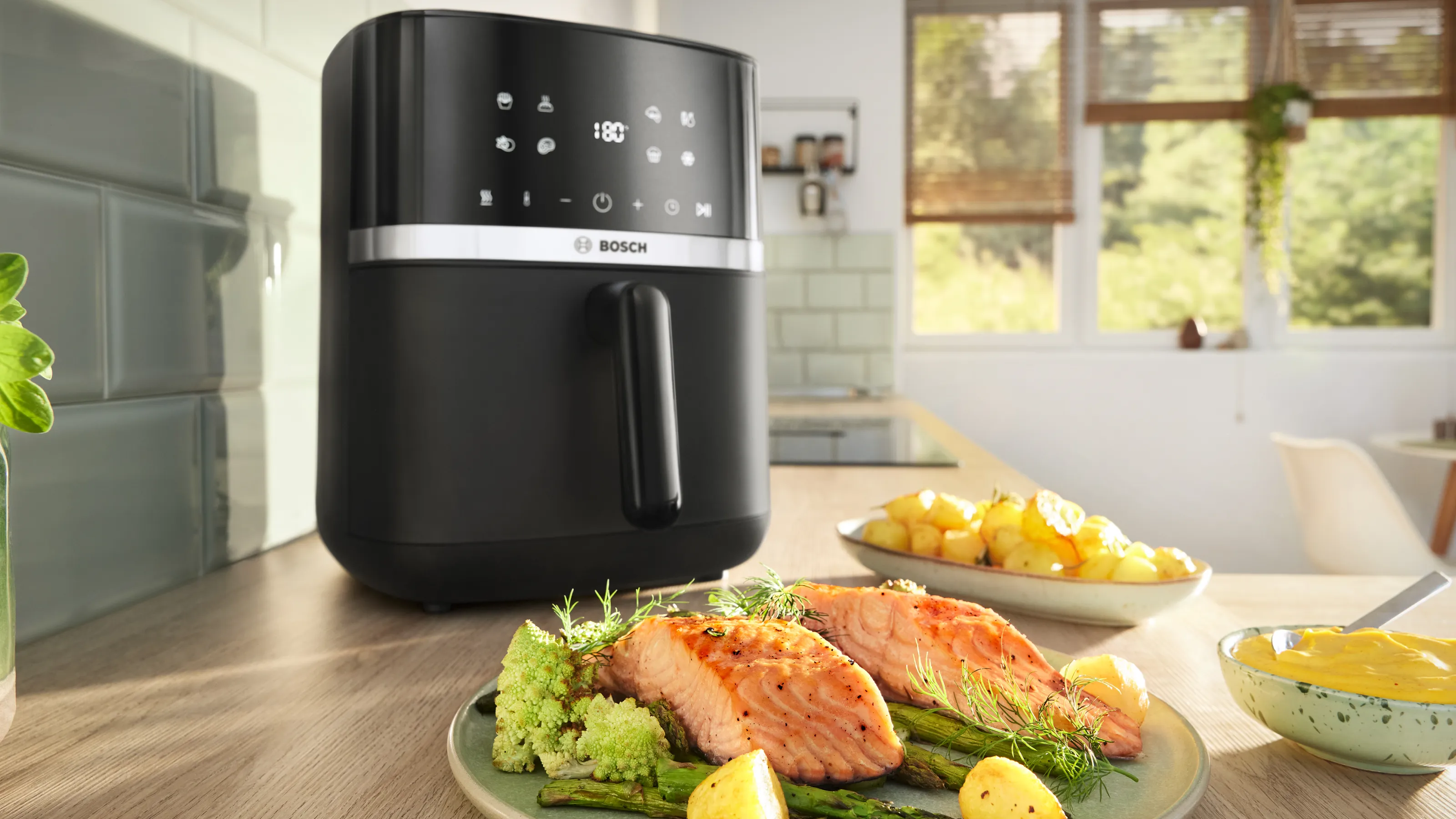 Air Fryer Bosch Serie 4, con davanti un piatto di salmone cotto, verdure e una salsa.