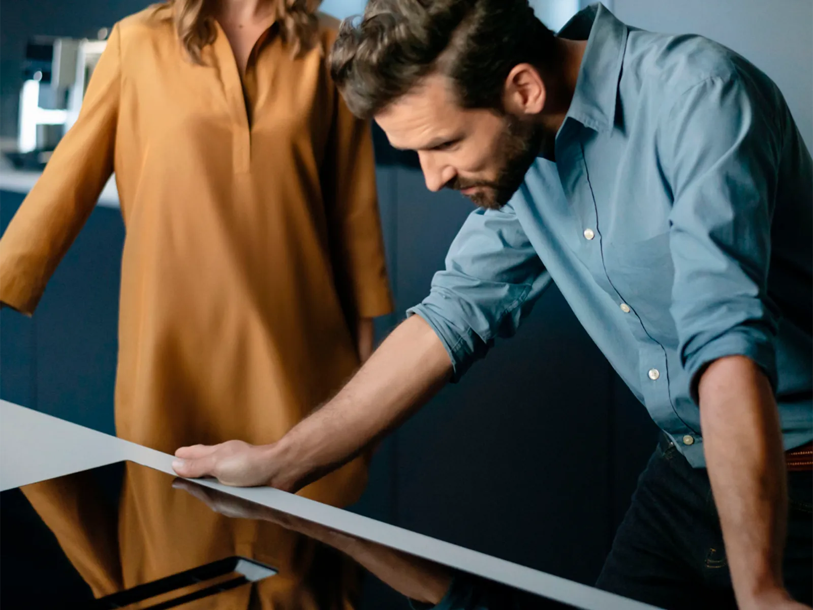 Um homem curvado sobre um fogão de indução Siemens e uma mulher ao fundo.