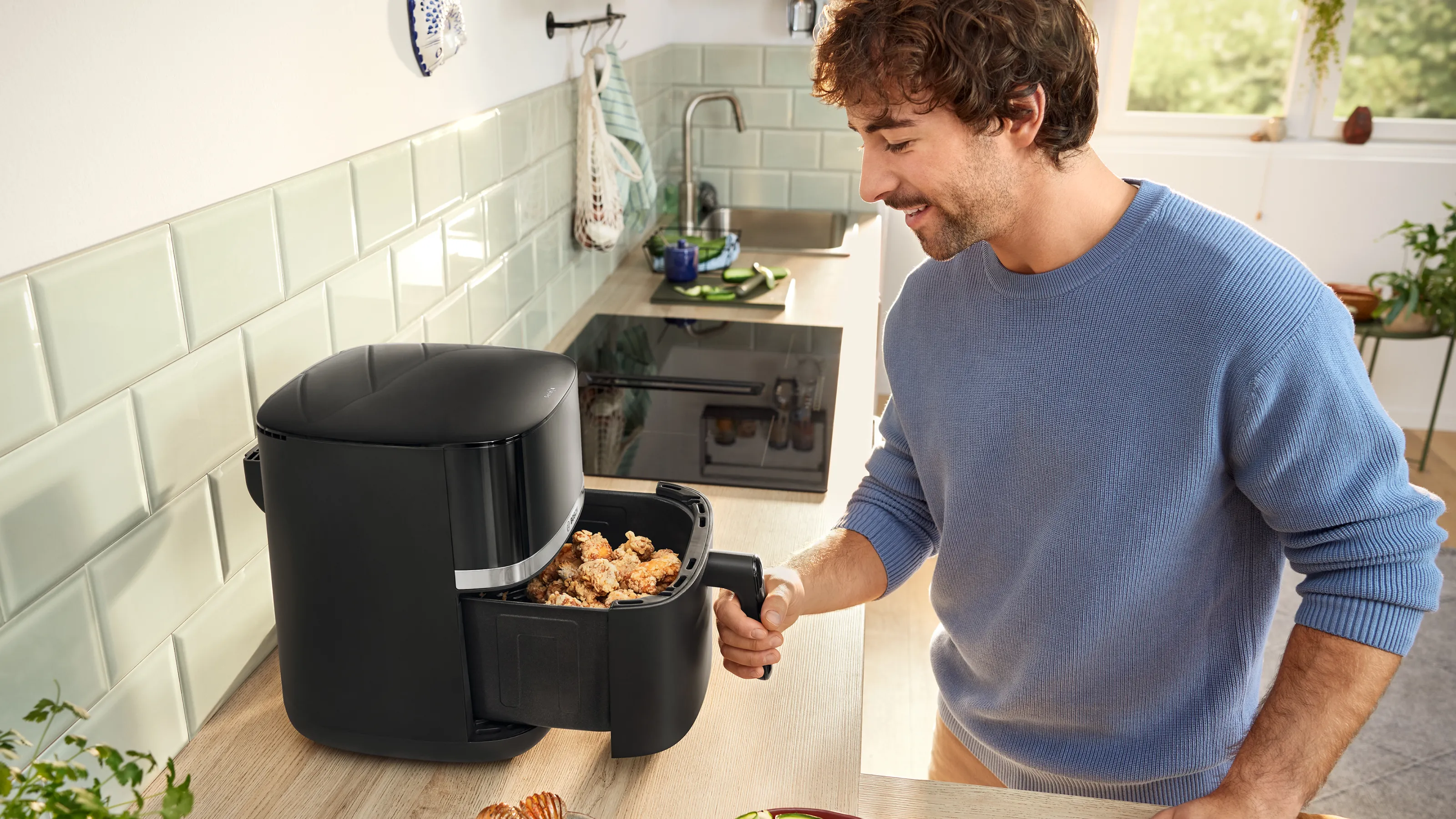 Un giovane in una cucina estrae parzialmente il cassetto del suo Air Fryer per controllare se il cibo è cotto.