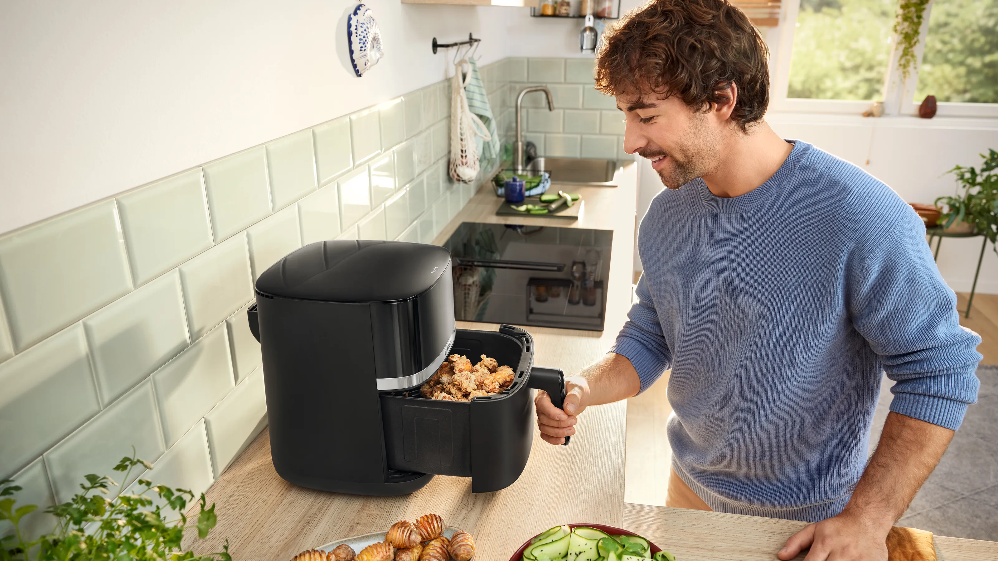 Un hombre sazonando pollo en una cocina, junto a una freidora de aire negra sobre la encimera.