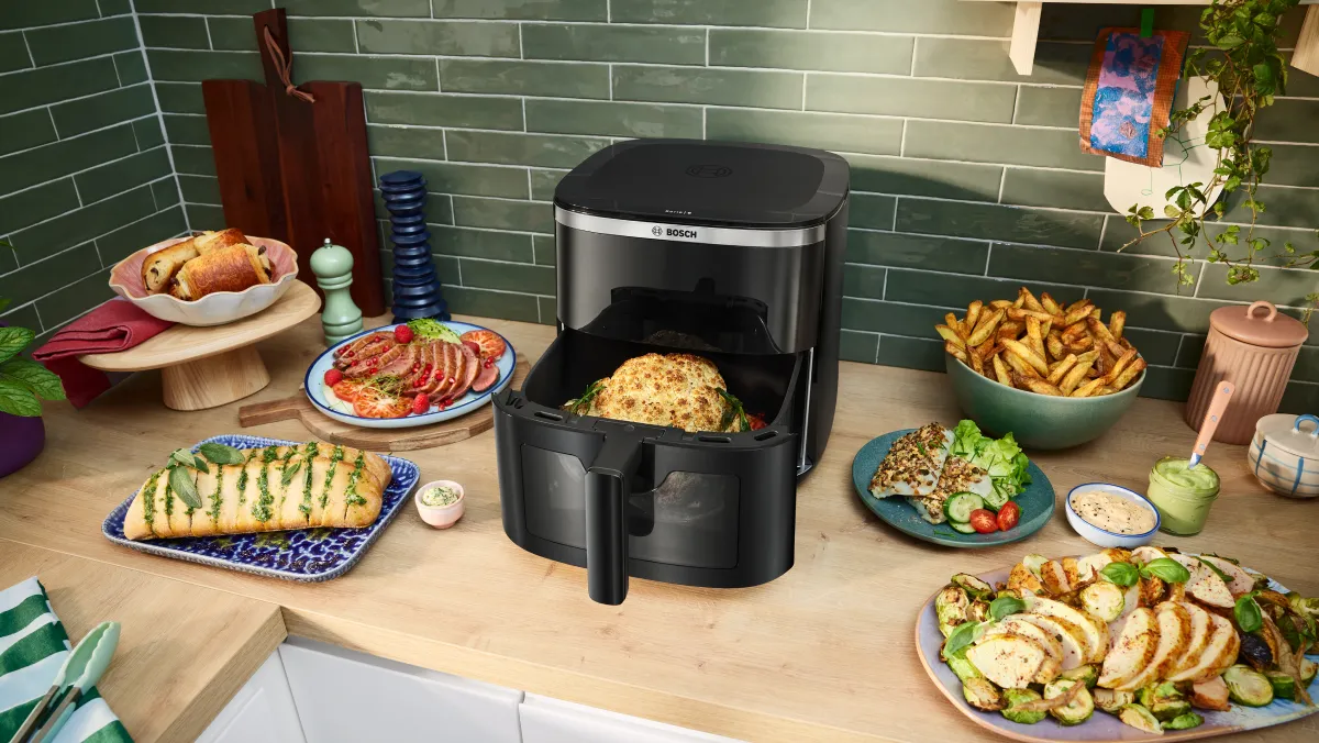 Een moderne airfryer op een aanrecht, omringd door verschillende bereide gerechten zoals kip, frietjes en groenteschotels.
