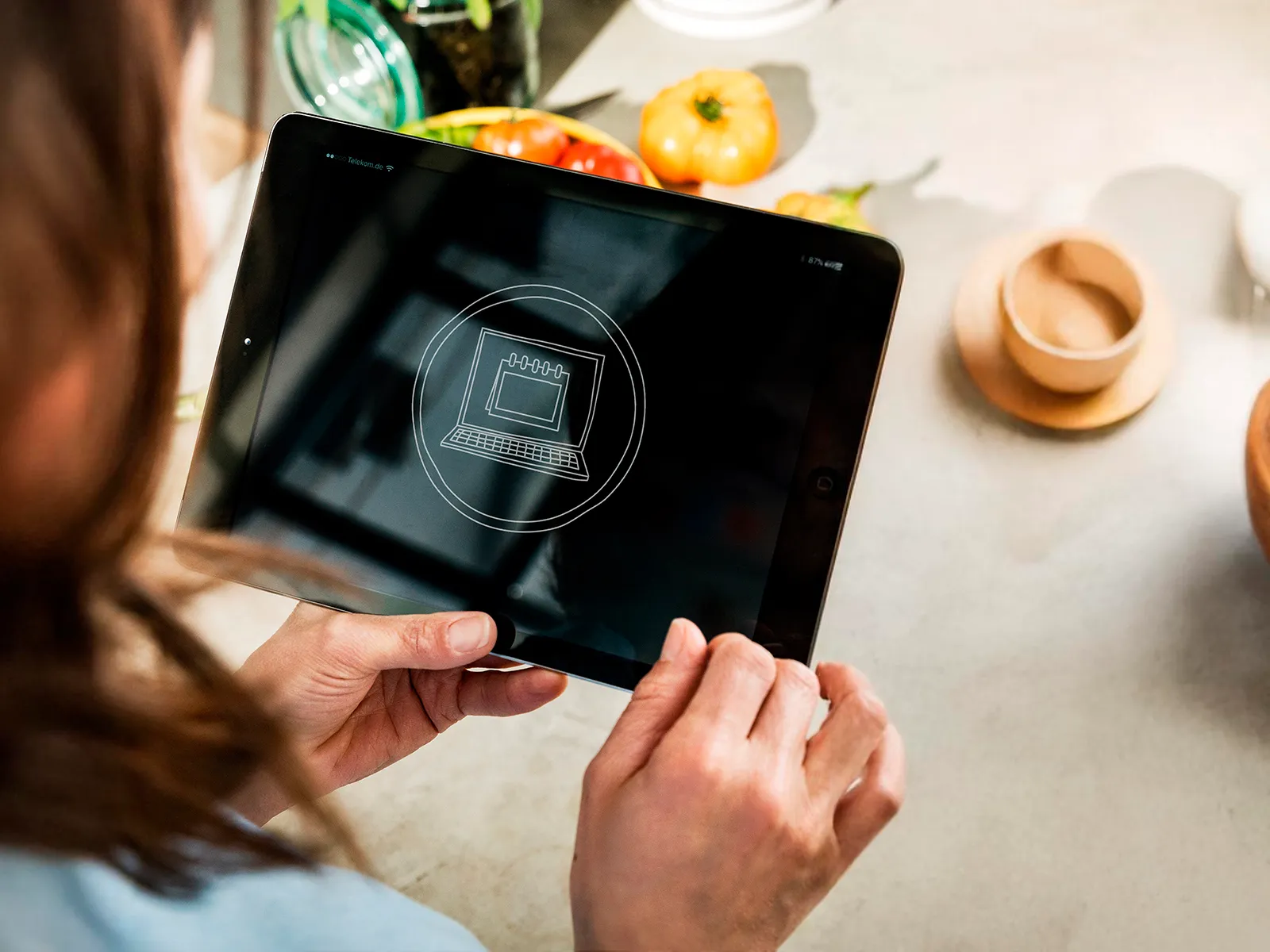 Person holding a tablet displaying a digital interface icon, with fresh vegetables in the background.