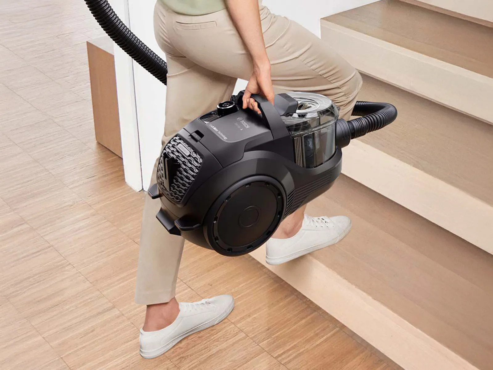 Woman climbs the stairs with a bagless cylinder model.