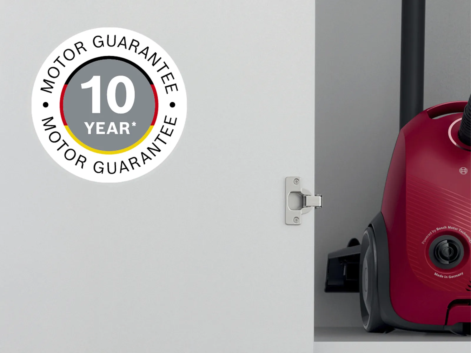 Red vacuum cleaner peeking behind a door with a '10 Year Motor Guarantee' sticker on it.