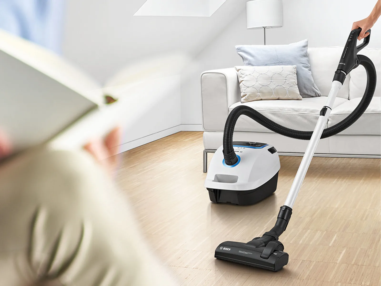  Osoba vysává podlahu, zatímco si někdo jiný poblíž čte.