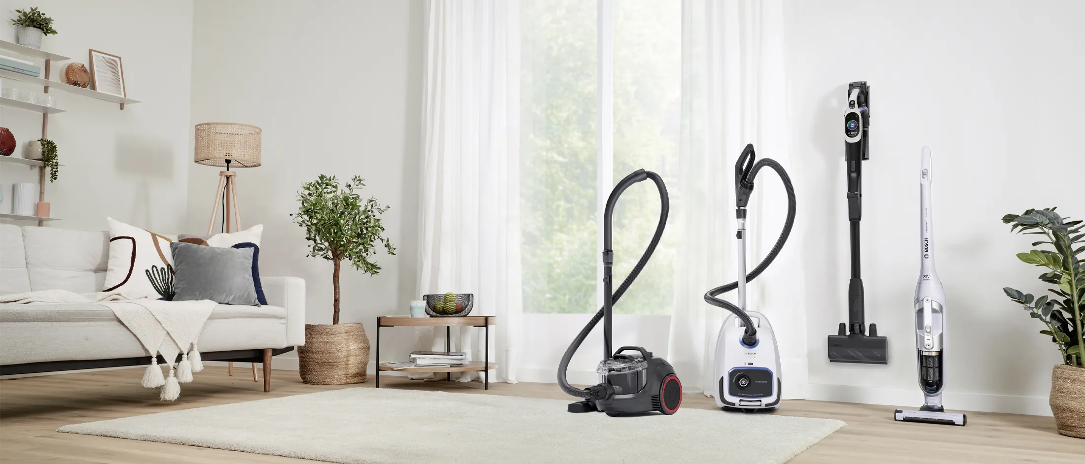 A lineup of four different vacuum cleaners in a bright hallway.
