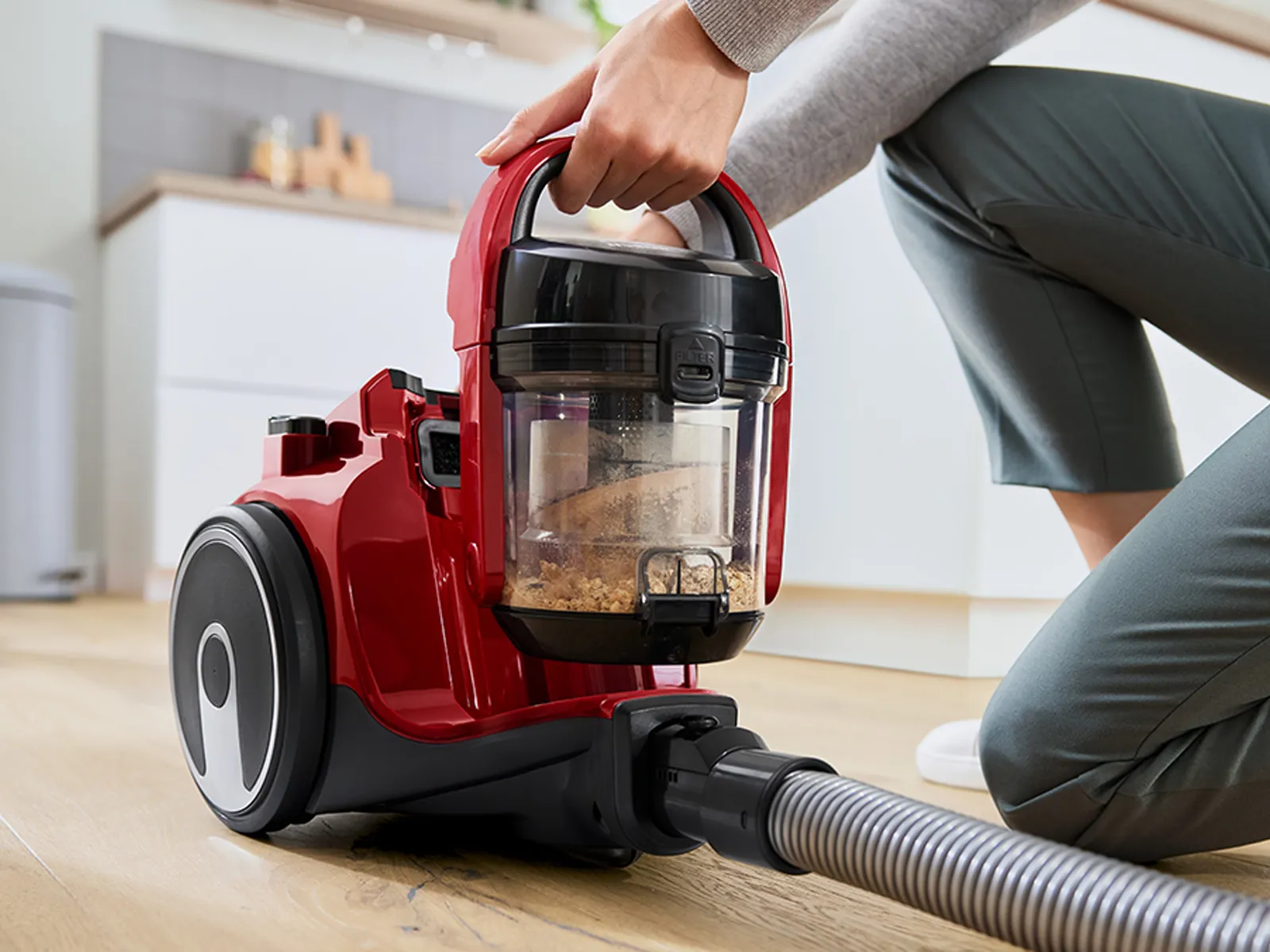 Person using a red canister vacuum cleaner on a wooden floor.
