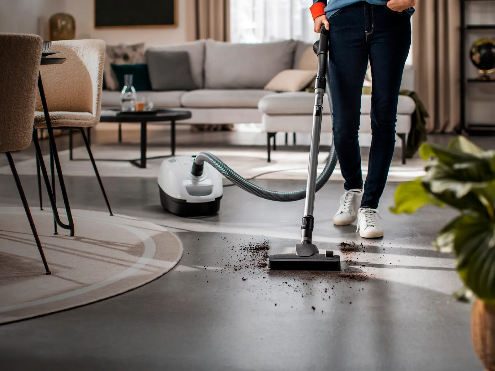 Person using a Siemens vacuum cleaner in a stylish living room, effortlessly cleaning dirt from the floor.