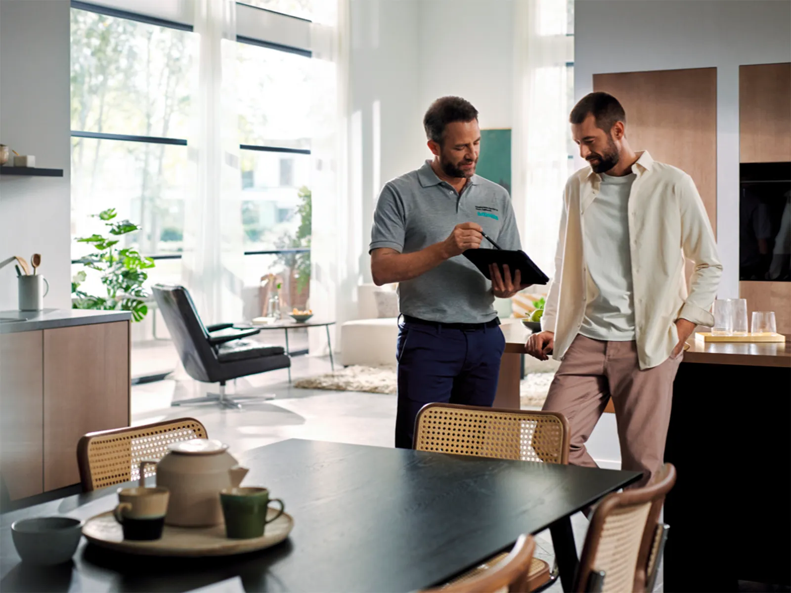 Siemens technician in a grey polo shirt explaining something on a tablet to a customer in a modern kitchen.