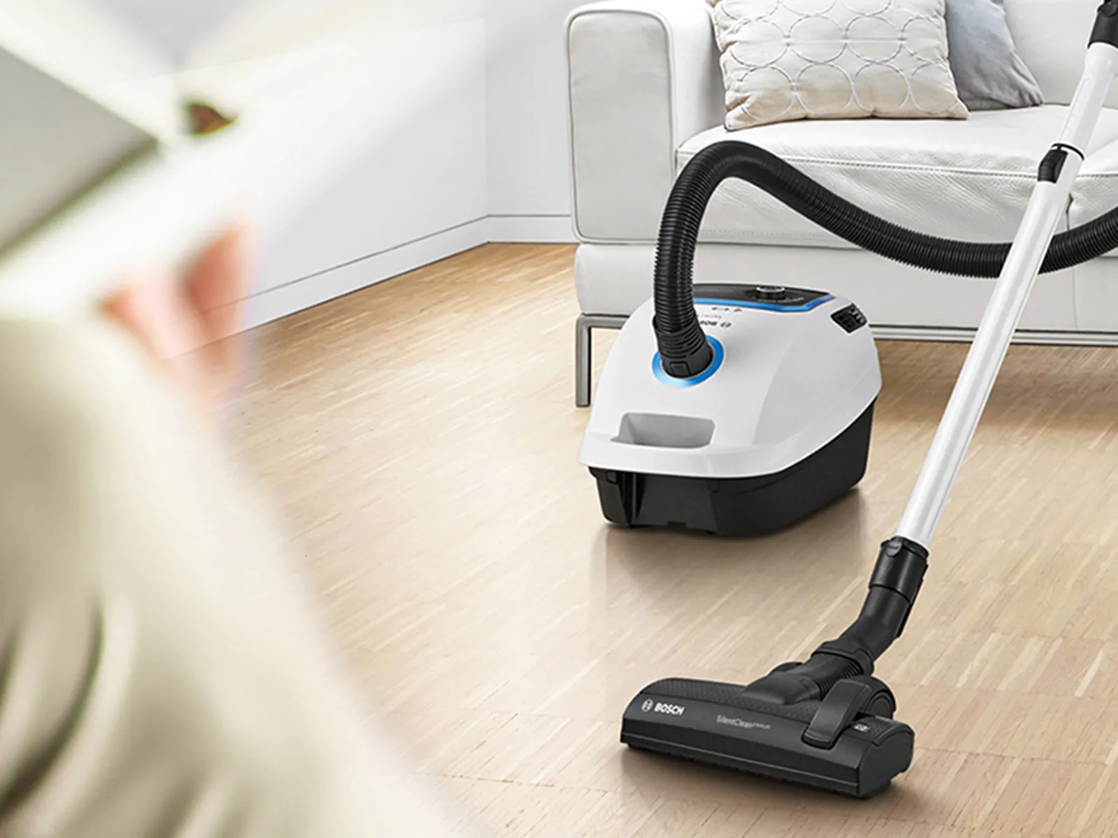 A person vacuums the floor while someone reads nearby.