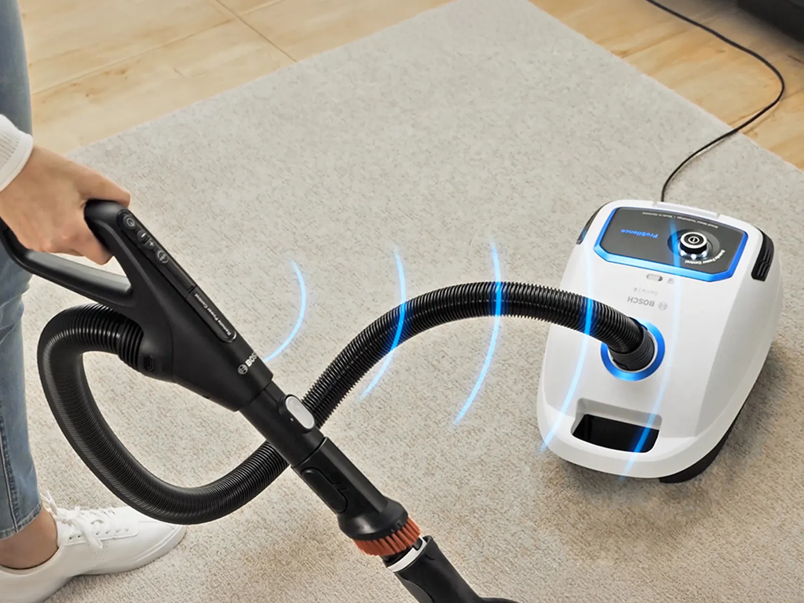 Blue lines indicating power emanate from a Bosch bagged vacuum that is being used to clean a rug.