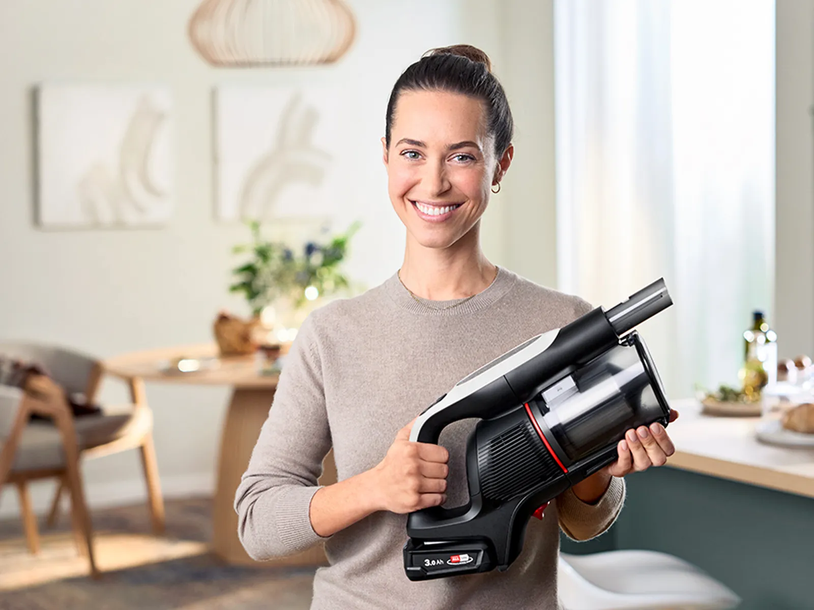 Eine Frau lächelt und hält einen Unlimited kabellosen Stabstaubsauger.