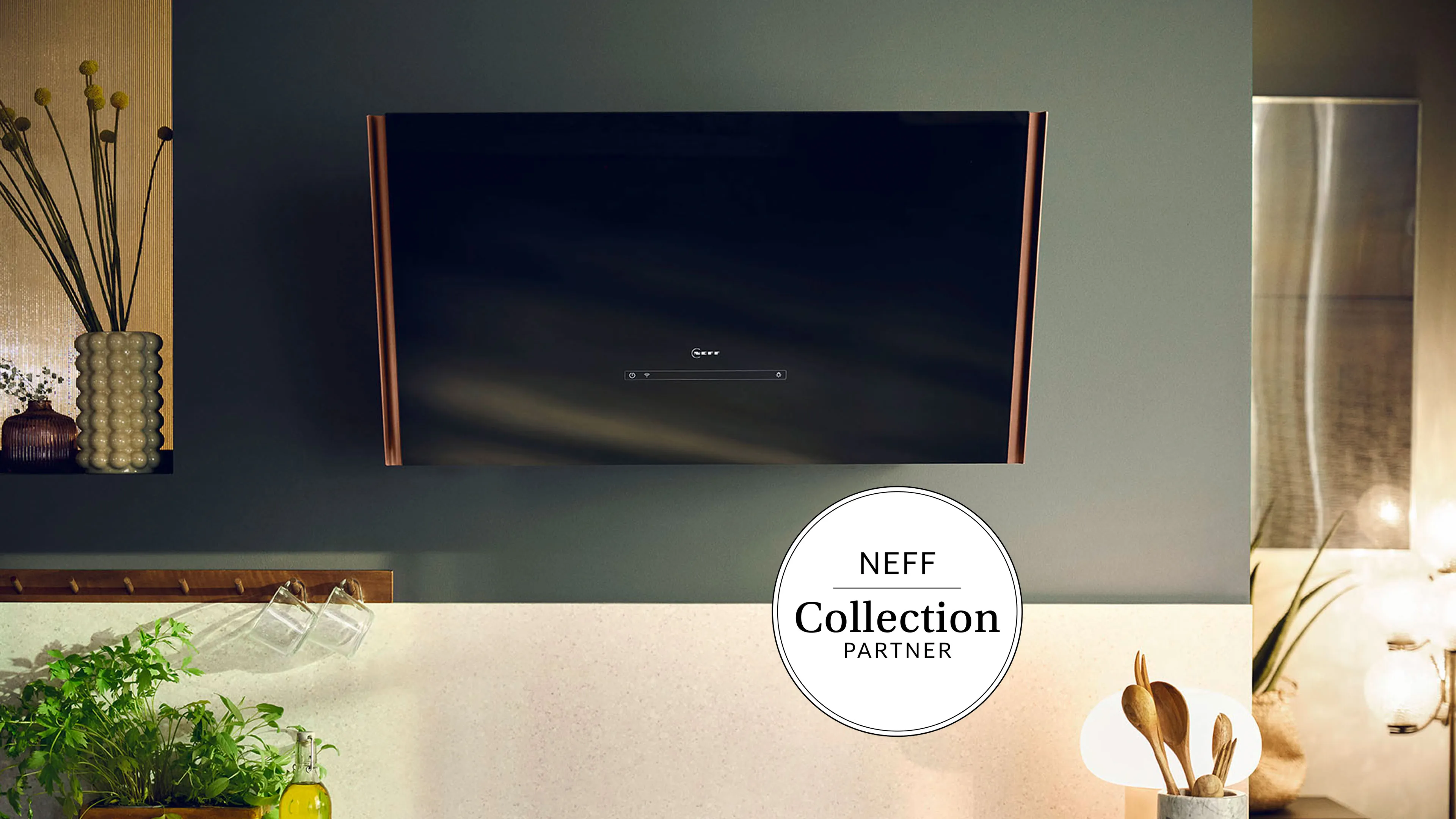 NEFF avtrekksvifte i svart glass med kobberlister montert på veggen og et NEFF Collection Partner-logo i nedre høyre hjørne.
