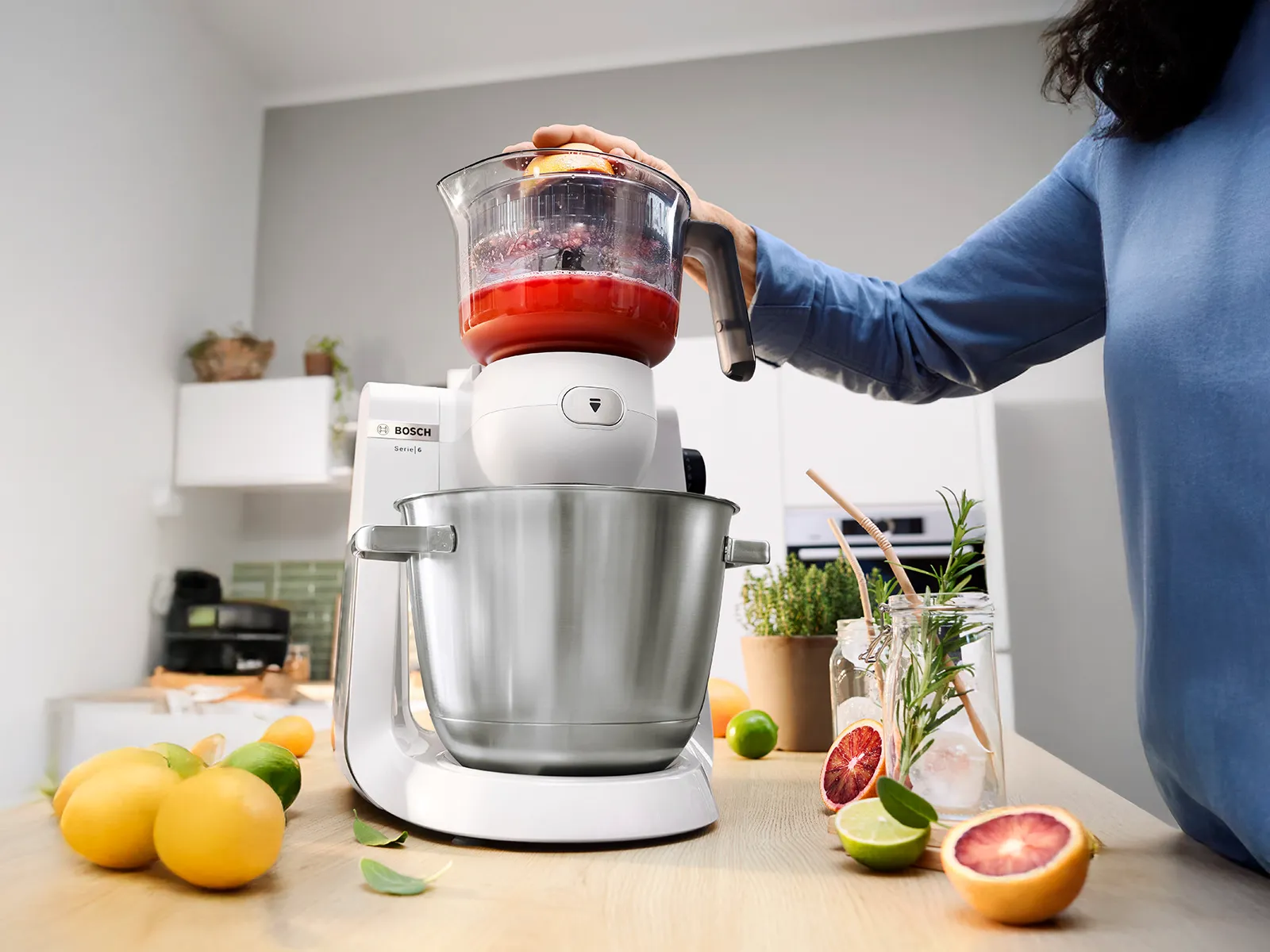 White Series 6 kitchen machine with citrus press accessory and hand squeezing pink grapefruit.