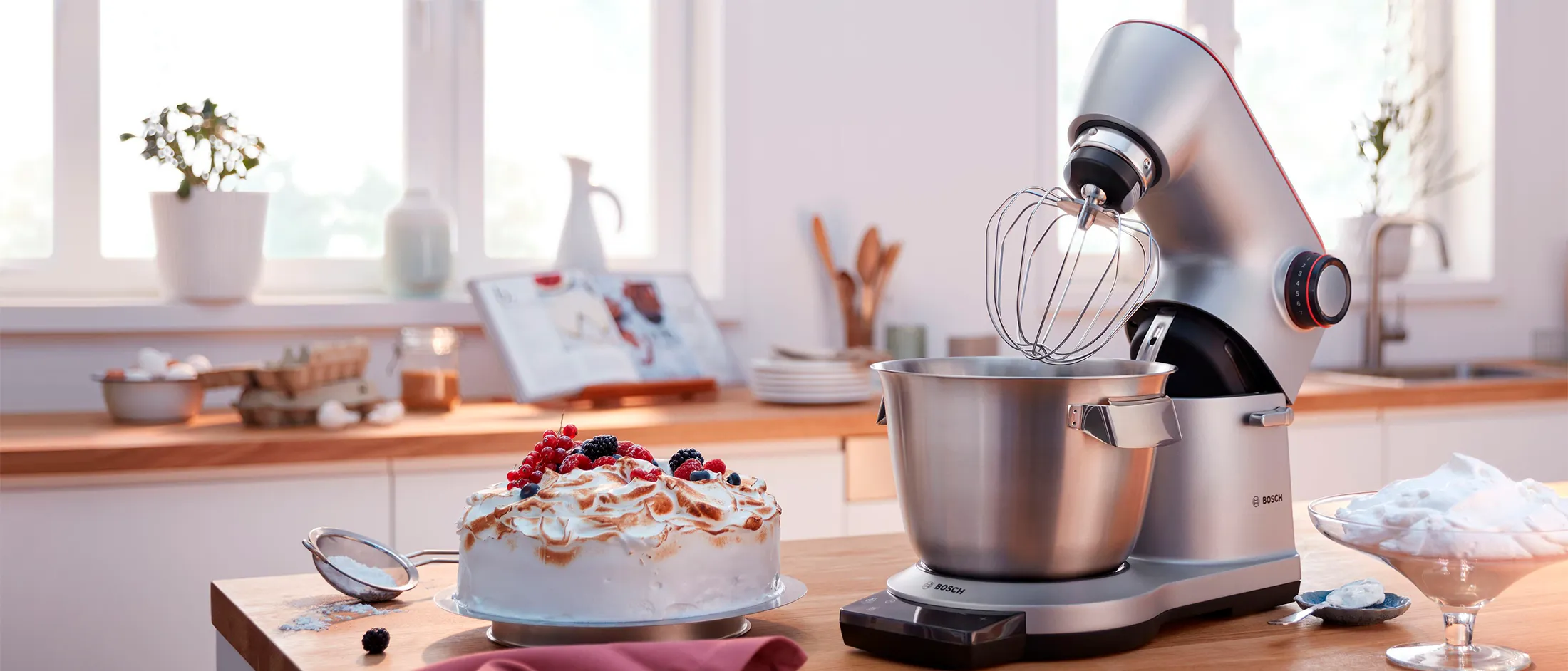 Bancada de cozinha com mesa de mistura, bolo e utensílios de cozinha.