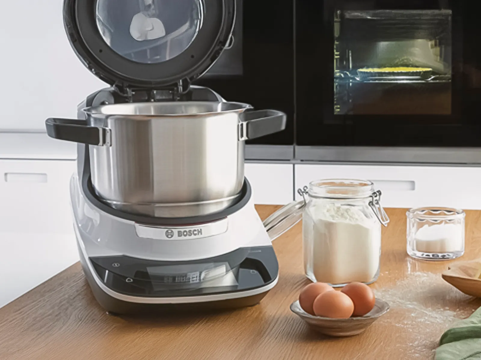 Bosch Cookit with the lid open on a worktop next to eggs, flour and other ingredients.