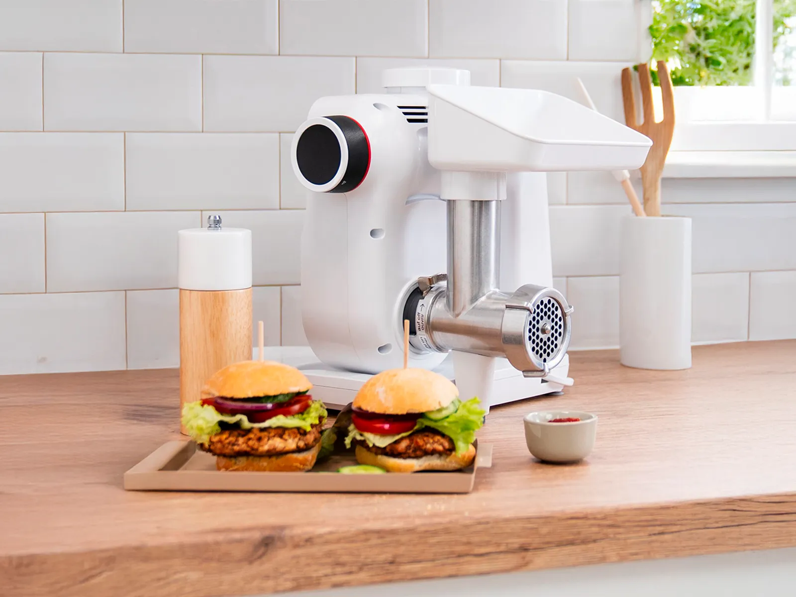 Deux hamburgers fraîchement préparés à côté d'un batteur sur socle Bosch avec un hachoir à viande.