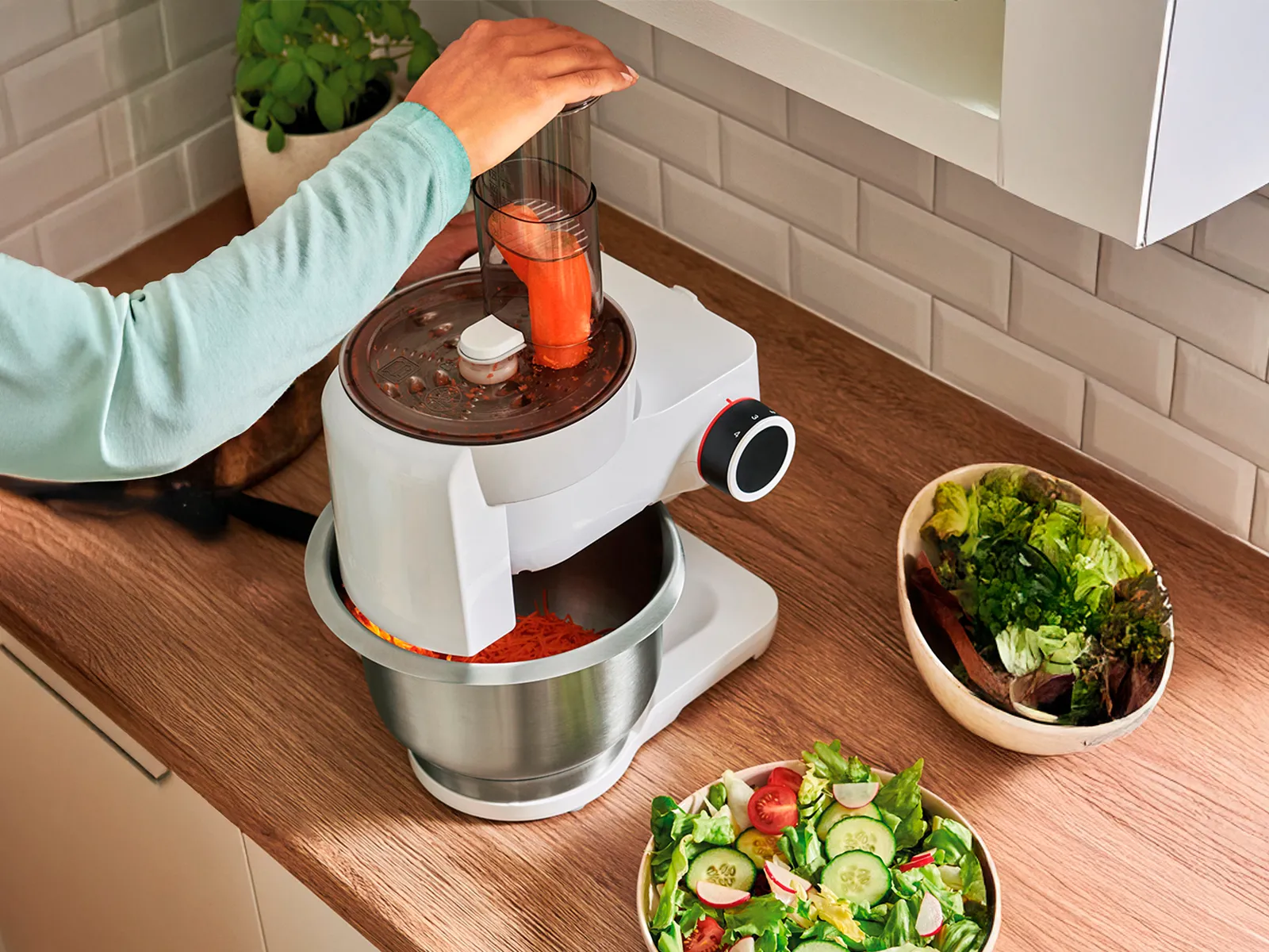 À l'aide d'un batteur sur socle Bosch, une personne prépare une salade fraîche dans une cuisine.