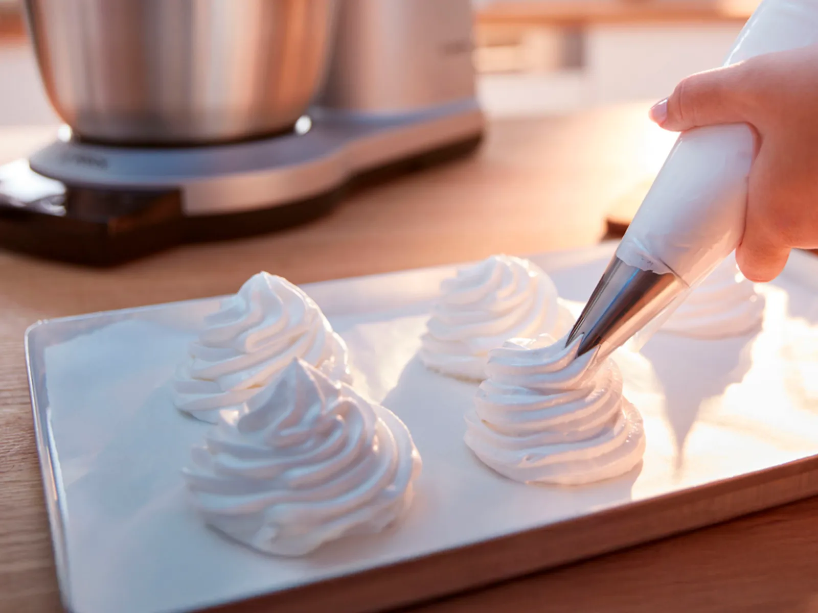 On voit une personne utiliser un pinceau à pâtisserie pour étaler de la crème fouettée, avec un batteur sur socle Bosch en arrière-plan