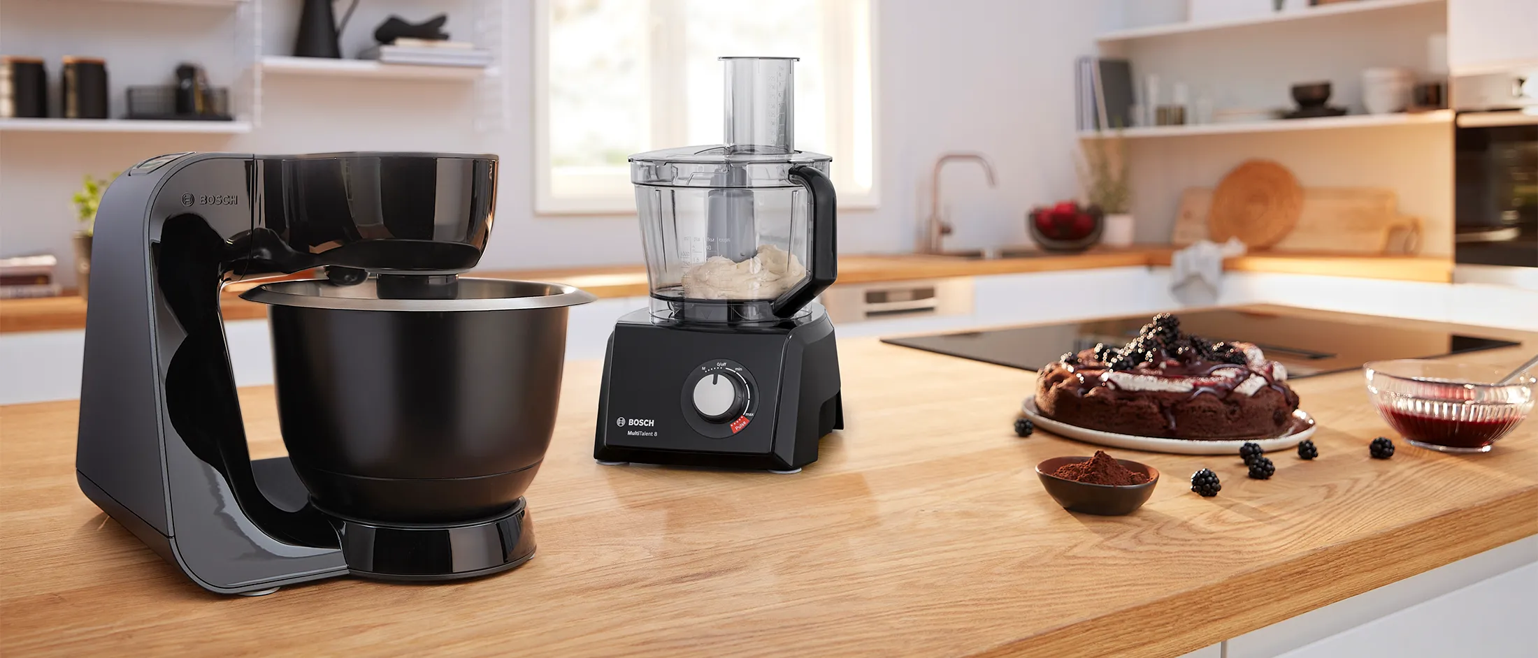 Robô de cozinha Bosch e processador de alimentos Bosch numa bancada de madeira ao lado de um bolo.