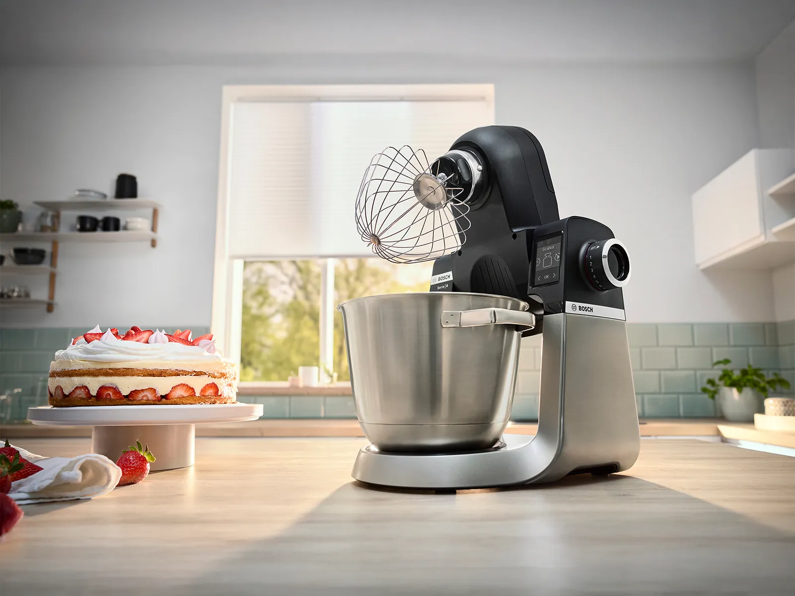 Bosch stand mixer with a whisk next to a cake and whipped cream.