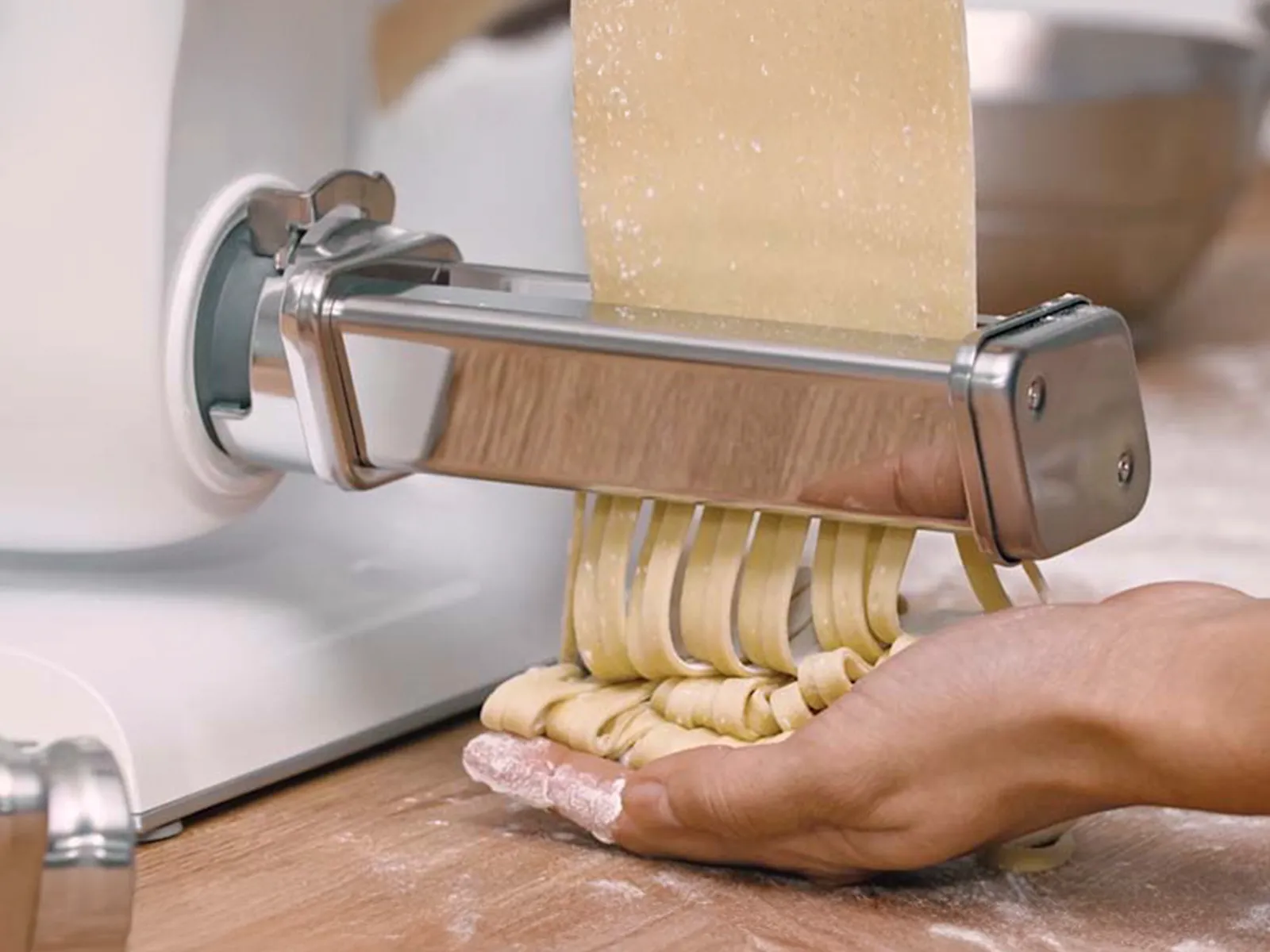 Close-up of stand mixer with PastaPassion attachment, with pasta being fed through to make tagliatelle.