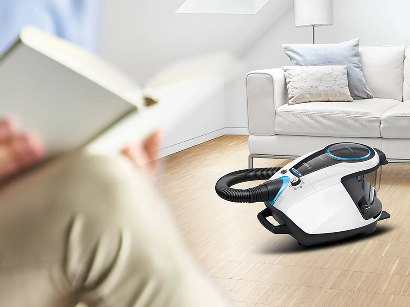 En person dammsuger golvet medan någon läser i närheten.