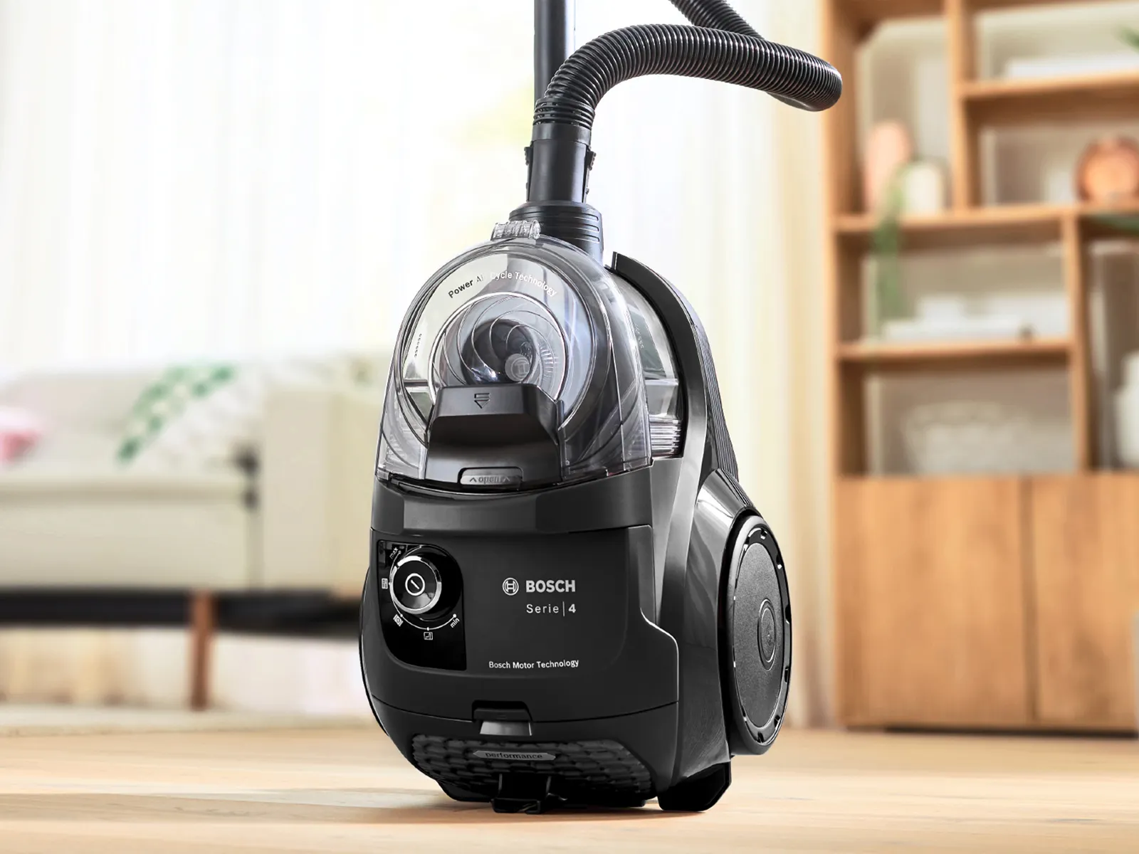 En Bosch cylinderdammsugare står upprätt framför ett skåp i ett vardagsrum.