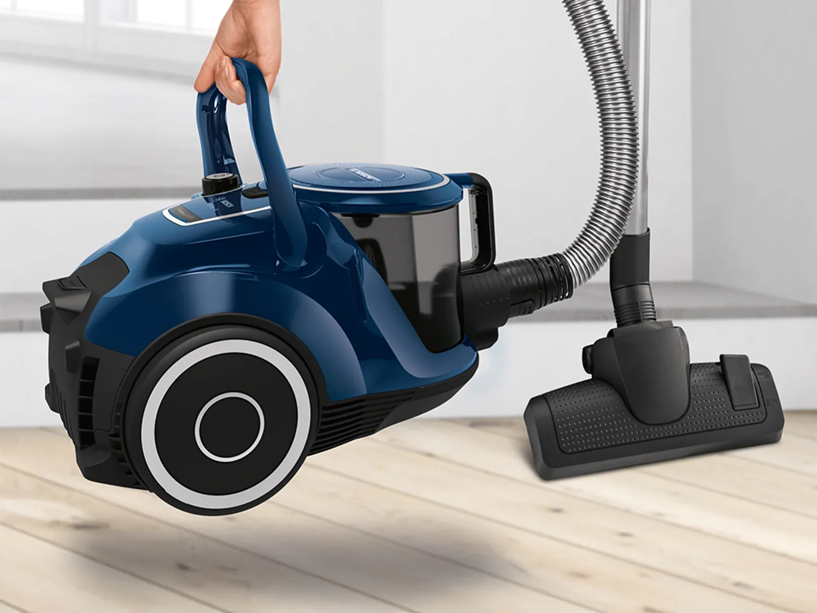 En hand plockar upp en blå cylinderdammsugare utan påse.