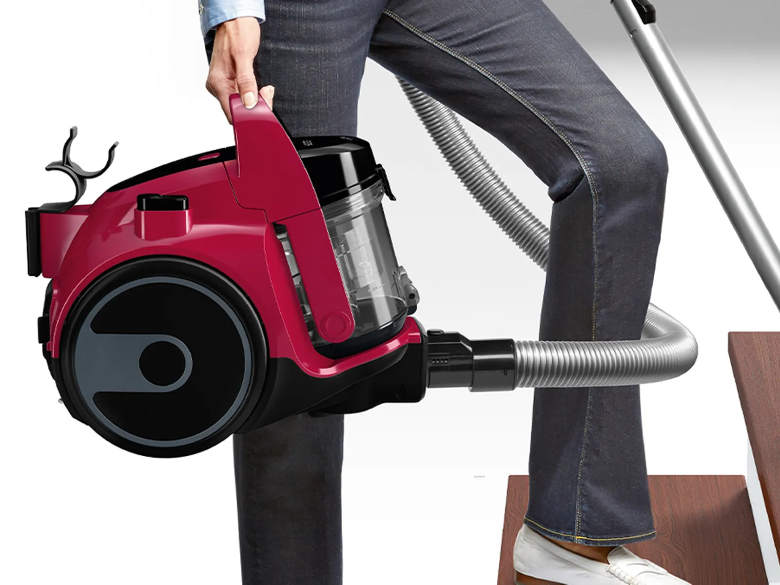 A person carries the red cyclinder of a Bosch bagless vacuum while cleaning stairs.