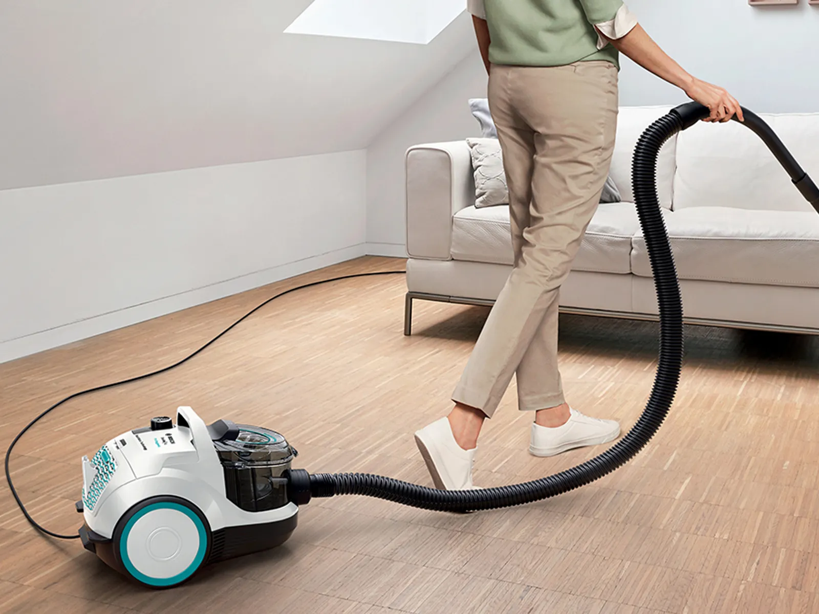 En person använder en Bosch påslös dammsugare för att städa ett litet loft med en soffa.