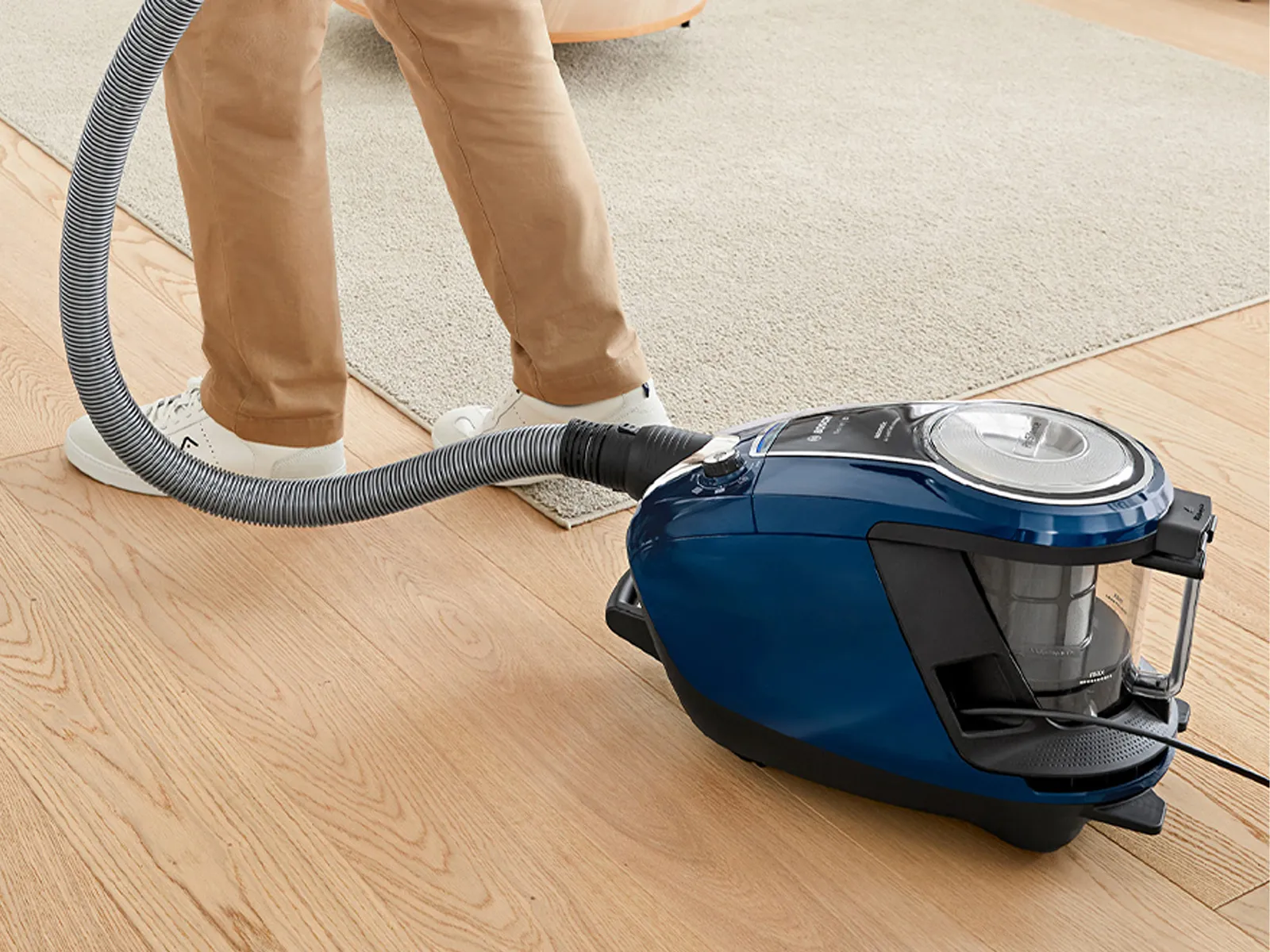 En person städar ett hårt golv med en Bosch påslös dammsugare.
