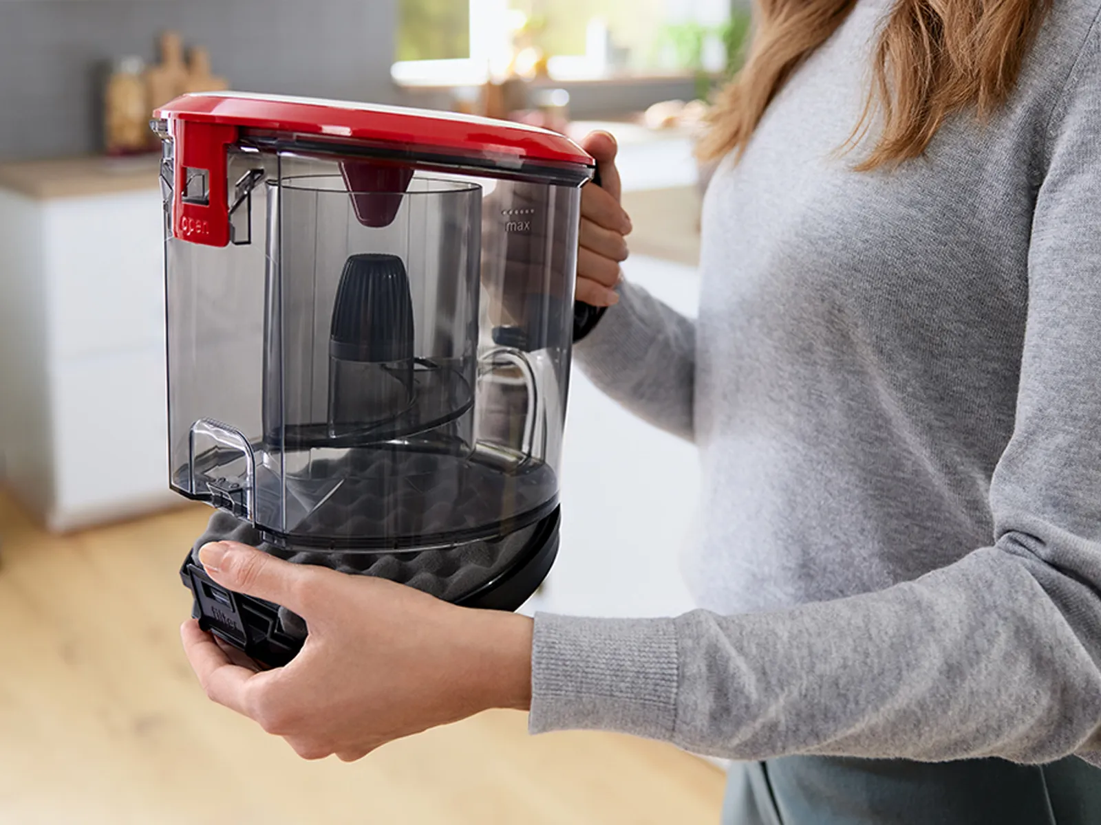 A woman lifts the dust box out from a canister vacuum cleaner.