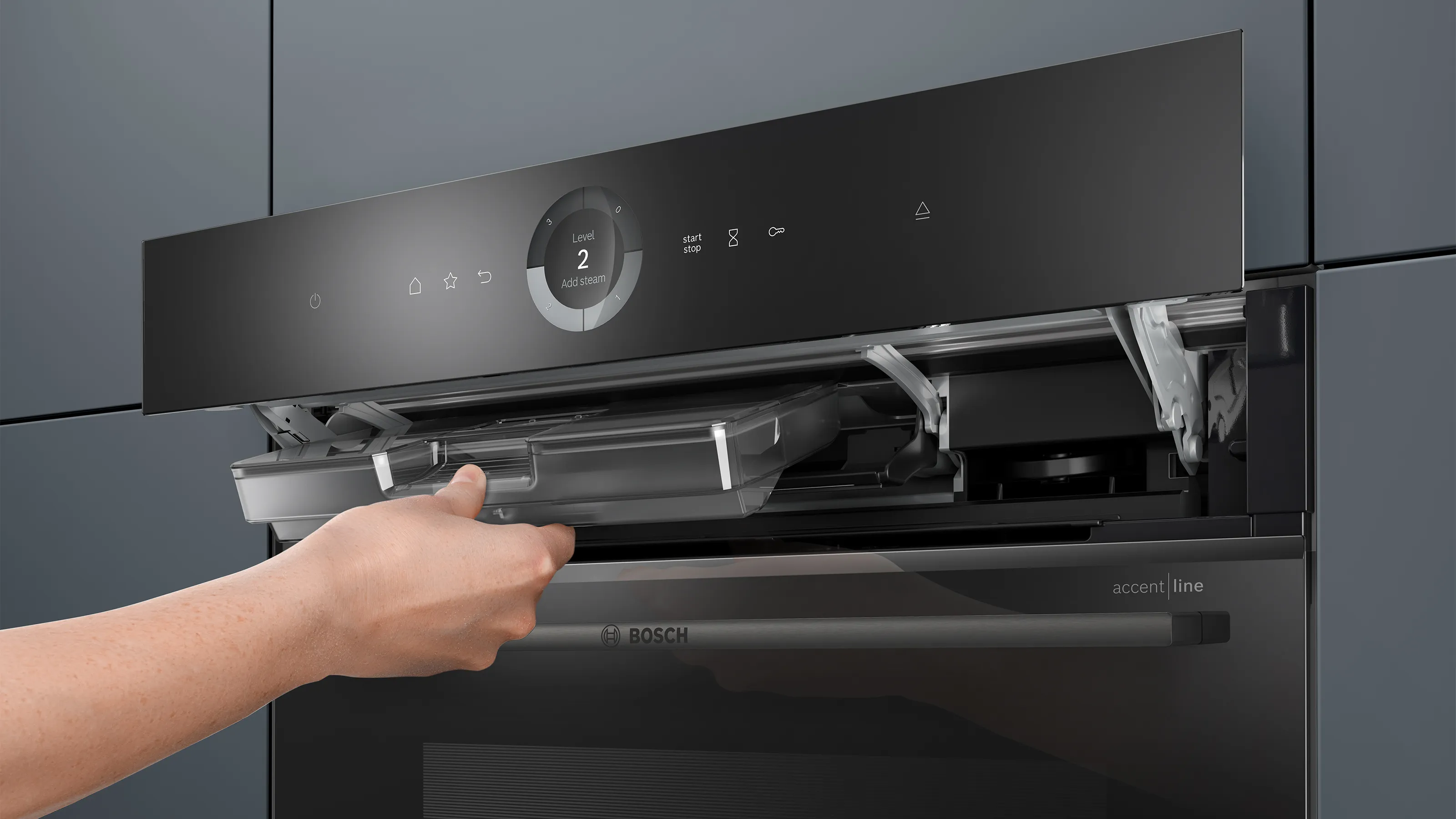 Eine Hand entnimmt den Wassertank hinter der automatisch hochfahrenden Bedienblende eines Bosch accent line Dampfbackofens.
