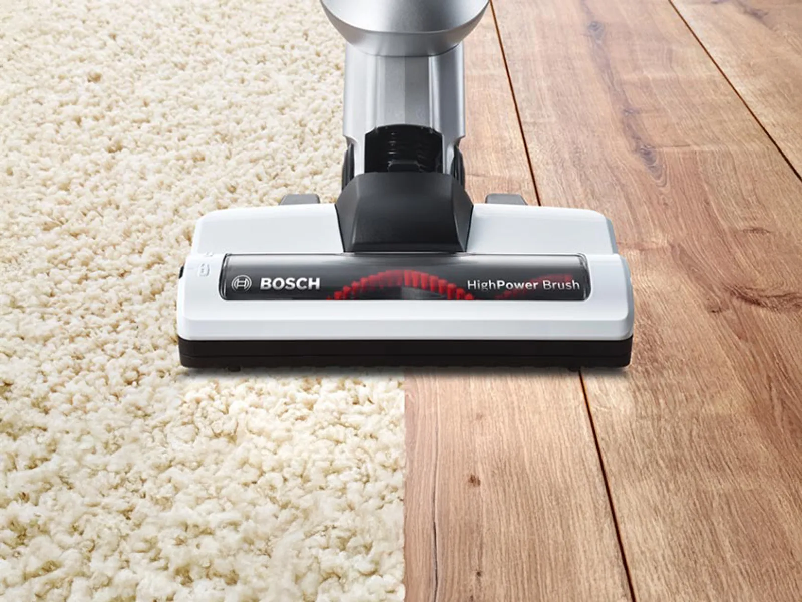 Une brosse d'aspirateur se déplace sur le tapis et le sol en bois.