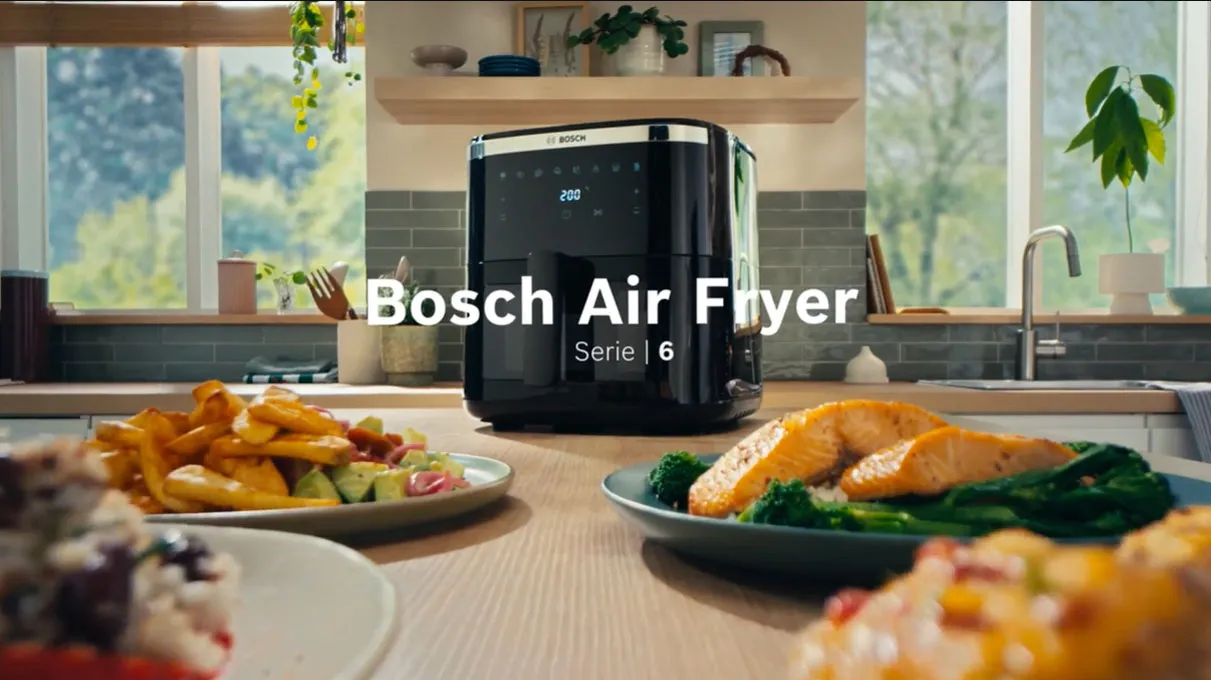 Friggitrice ad aria calda Bosch Serie 6 con vari piatti, posizionata su un piano di lavoro in legnoFriggitrice ad aria calda Bosch Serie 6 con vari piatti, posizionata su un piano di lavoro in legno