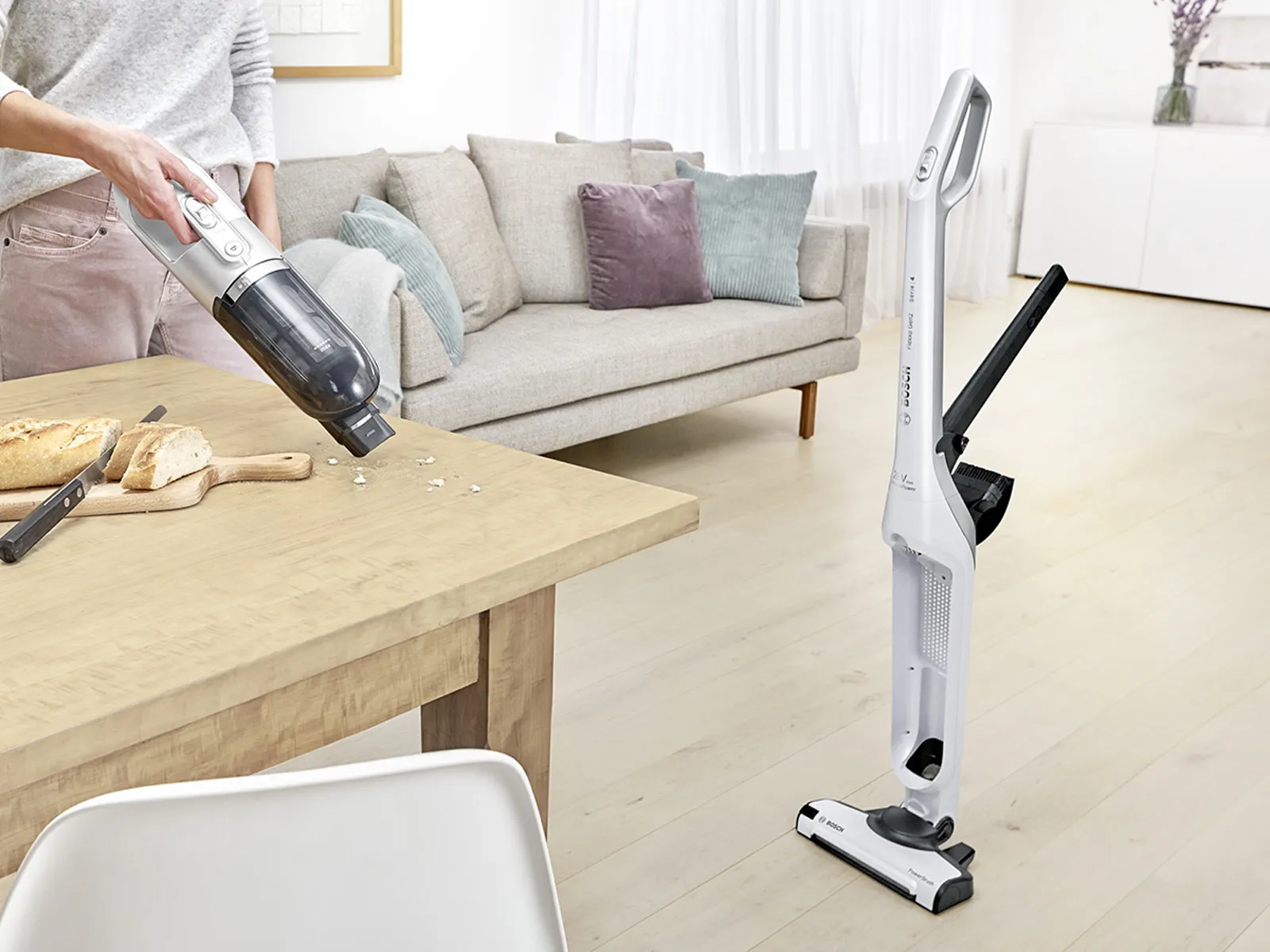 Bezdrátový vysavač Flexxo stojí uprostřed místnosti, viditelné jsou integrované příslušenství.
