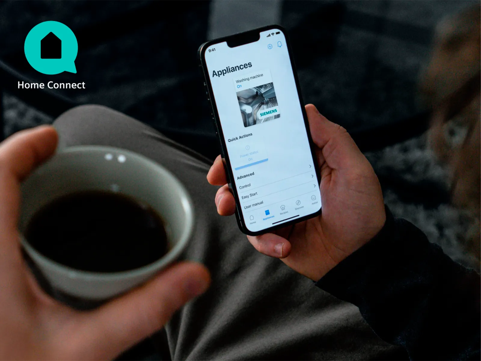 Person holder smartphone med app til husholdningsapparater og en kaffekop.