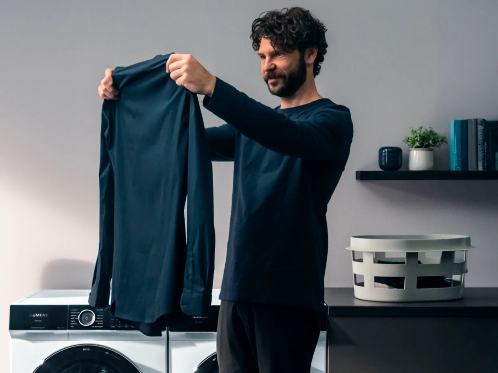 Person, der holder en blå skjorte foran en vaskemaskine i et moderne vaskerum.
