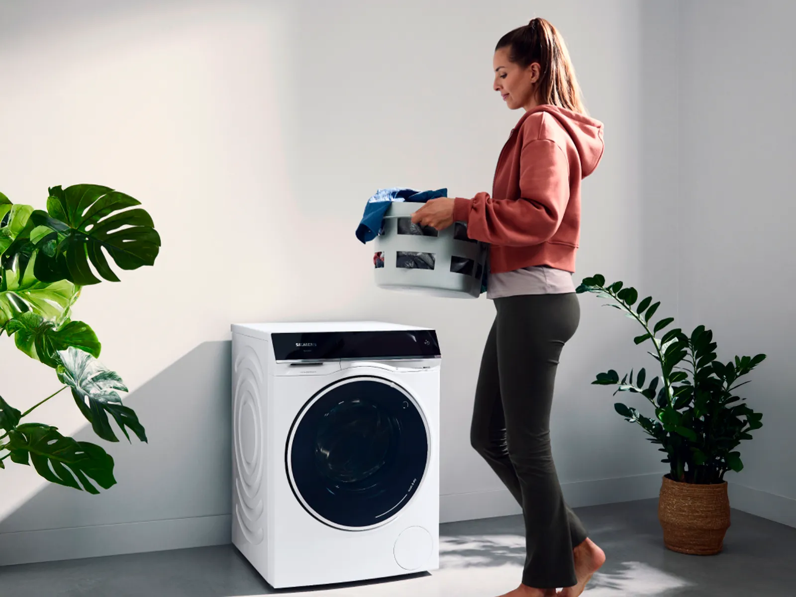 Mulher a carregar um cesto de roupas para a máquina de lavar.