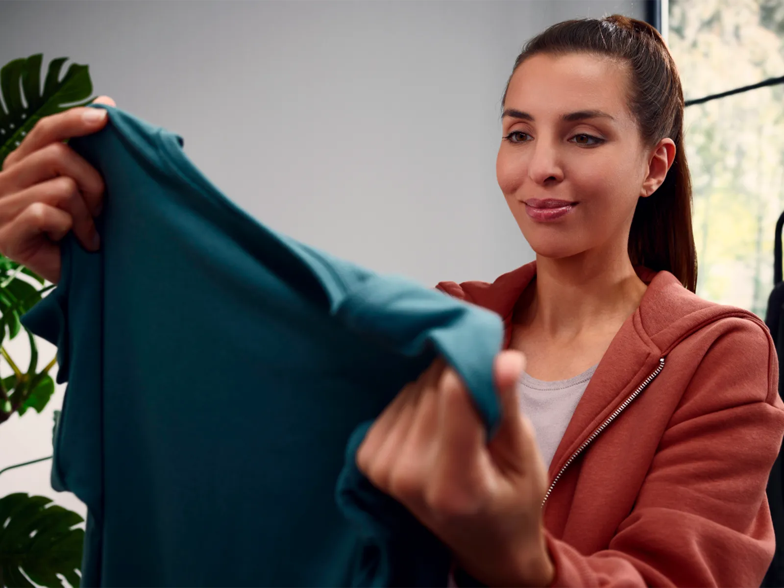 Pessoa a segurar uma camisa azul com um cabideiro ao fundo.