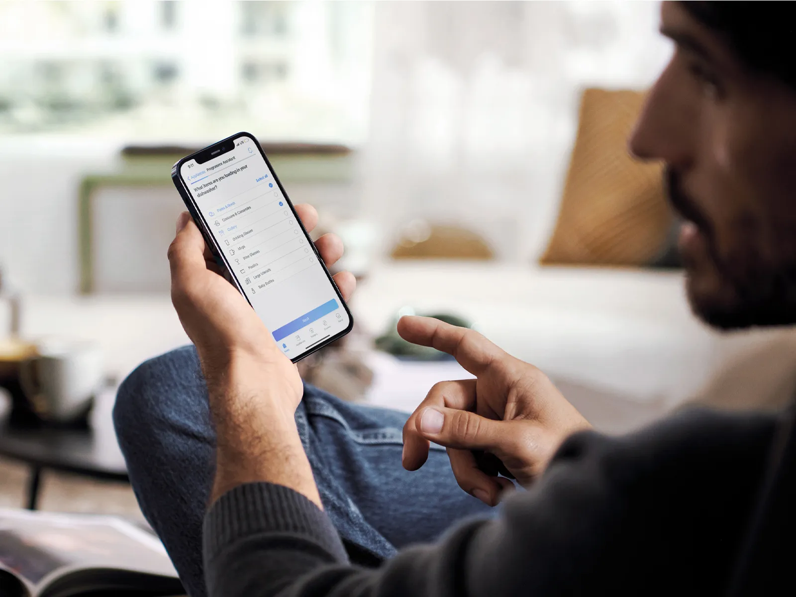 Person holding a smartphone with screen visible, sitting with crossed legs indoors.