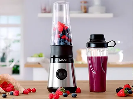 Bosch Miniblender VitaPower Series 2 with red fruits and a smoothie-filled To-Go-bottle on a kitchen shelf.