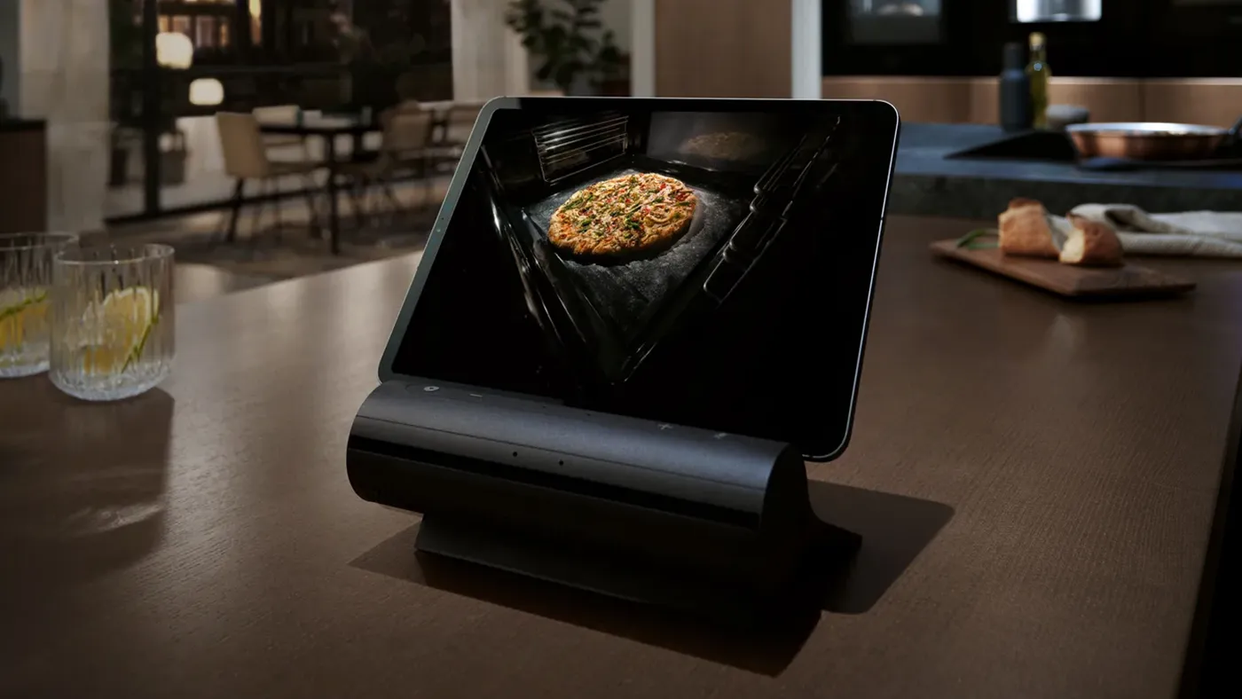 A tablet in a docking station on a countertop displaying a photo of a pizza inside an iQ700 oven.