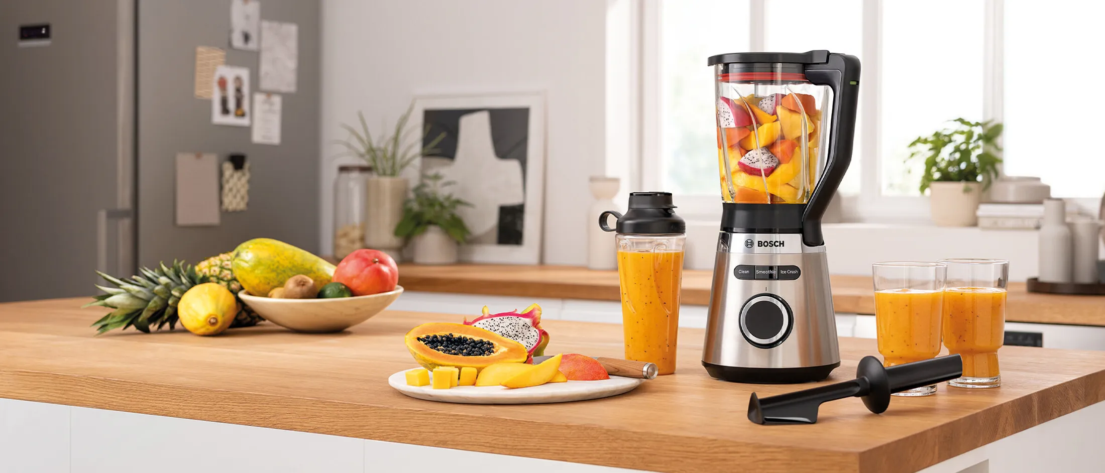Liquidificador Bosch VitaPower Serie 4 com frutas, garrafa To-Go e copos de smoothie em uma prateleira da cozinha.