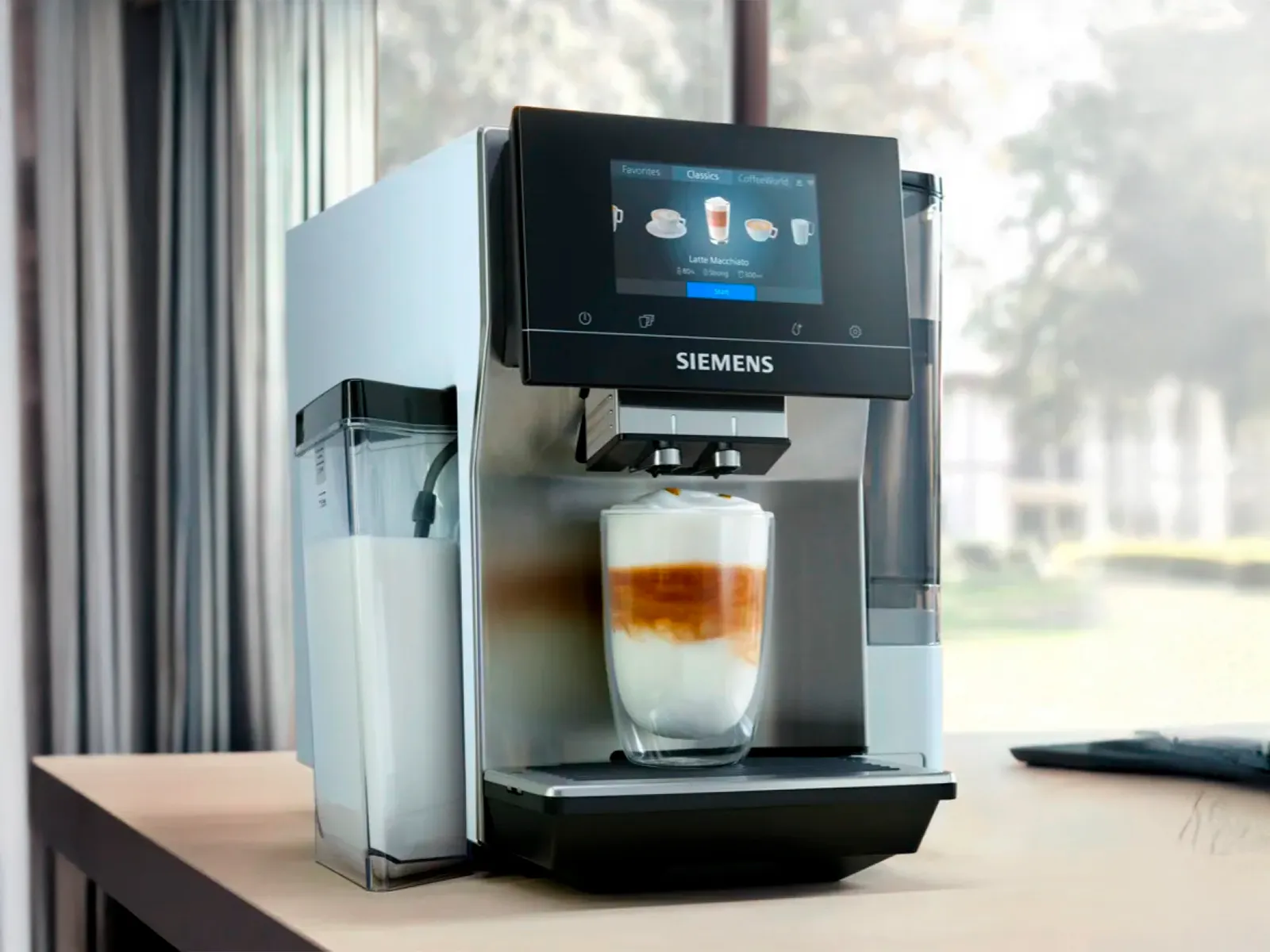 En Siemens kaffemaskine med touchskærm, der dispenserer en lagdelt latte macchiato i et klart glas.