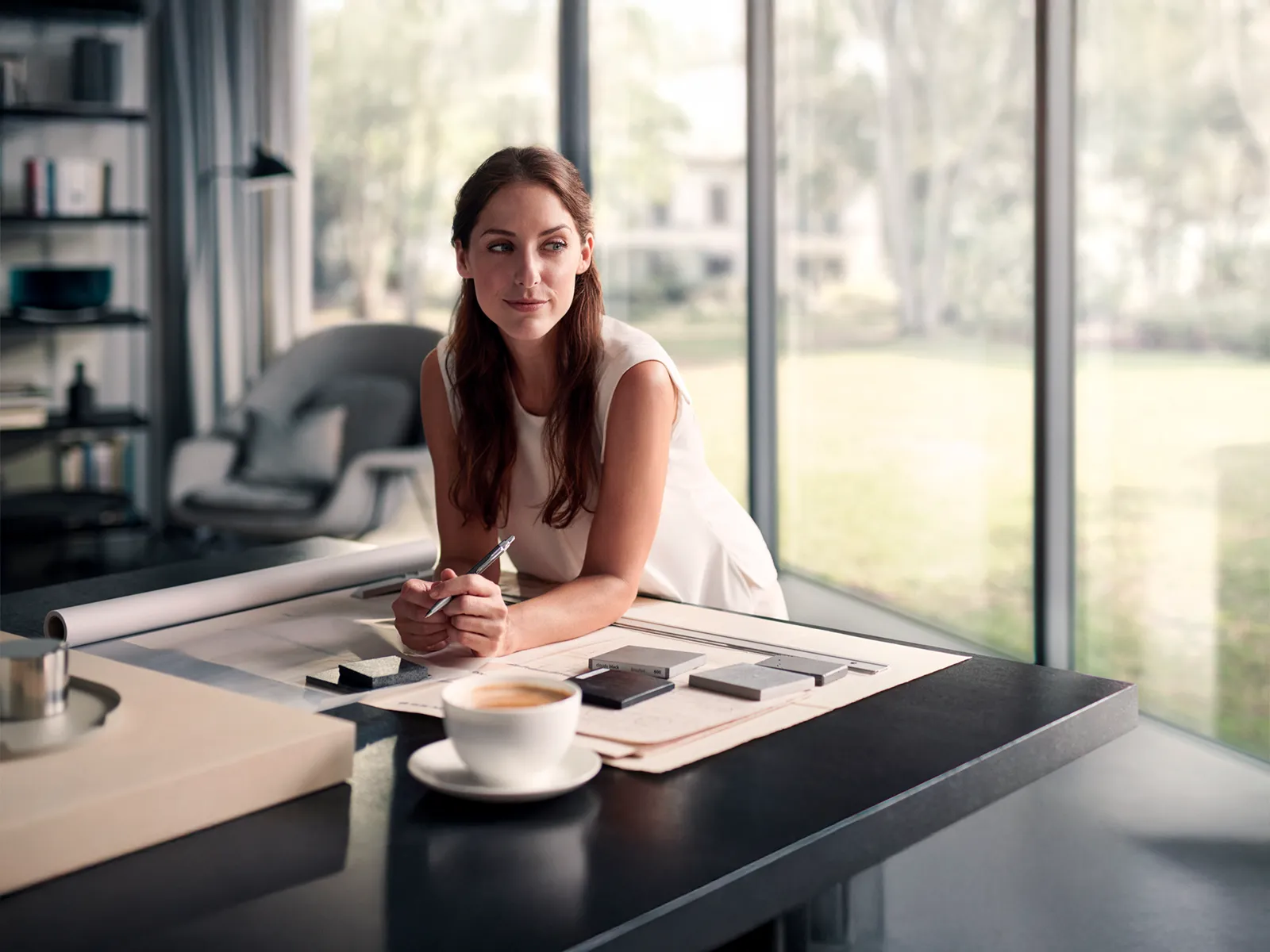 Kvinne som jobber med arkitektoniske planer med kaffe på bordet.