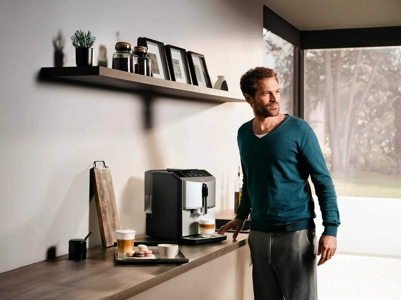 En mand står ved køkkenbordet og tilbereder en cappuccino med den fuldautomatiske espresso-/kaffemaskine EQ300.