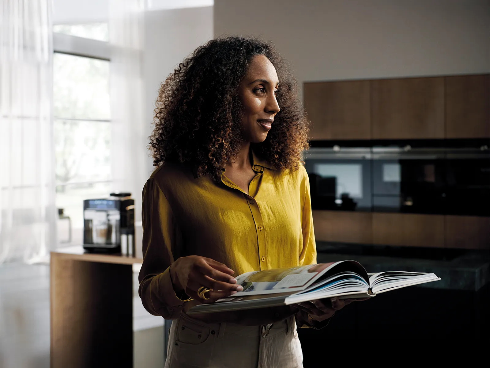 Kvinde læser en opskriftbog i et moderne køkken med en Siemens kaffemaskine i baggrunden.